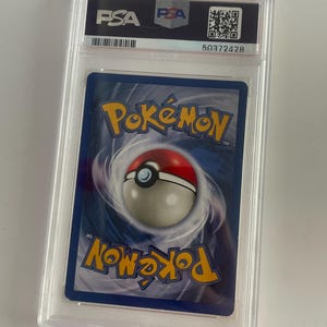 Puede incluir: Una carta coleccionable de Pok&eacute;mon calificada, encapsulada en un estuche de pl&aacute;stico transparente. El reverso de la carta presenta un fondo azul con el logotipo de Pok&eacute;mon y un dise&ntilde;o de Pok&eacute; Ball. El estuche tiene una etiqueta PSA con un c&oacute;digo QR y un n&uacute;mero de serie.