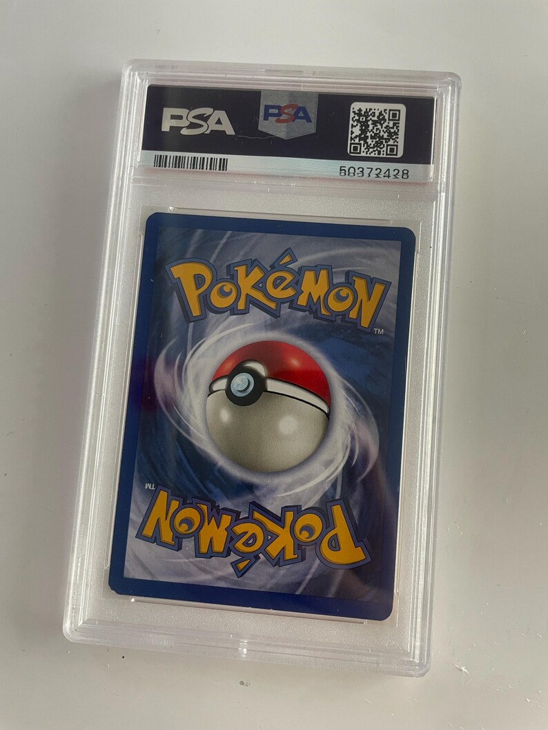 Puede incluir: Una carta coleccionable de Pok&eacute;mon calificada, encapsulada en un estuche de pl&aacute;stico transparente. El reverso de la carta presenta un fondo azul con el logotipo de Pok&eacute;mon y un dise&ntilde;o de Pok&eacute; Ball. El estuche tiene una etiqueta PSA con un c&oacute;digo QR y un n&uacute;mero de serie.