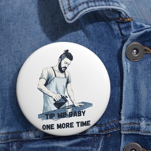 May include: White button featuring a barista pouring coffee, with the text "TIP ME BABY ONE MORE TIME". The illustration is in black and white, set against a blue denim jacket.