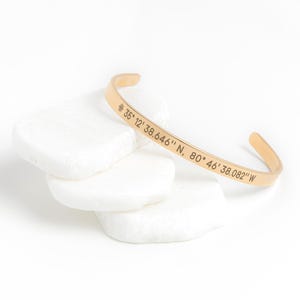 May include: Gold-toned bangle bracelet with engraved coordinates: 36° 12' 38.646" N, 80° 46' 38.082" W.