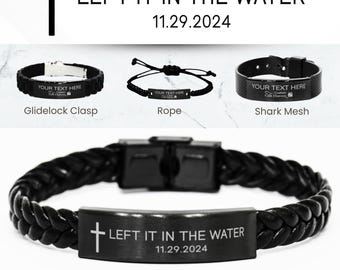 Könnte beinhalten: Schwarzes Lederarmband mit geflochtenem Design und einer silbernen Metallplatte, die mit einem Kreuz und dem Text "LEFT IT IN THE WATER 11.29.2024" graviert ist. Das Armband ist ein personalisiertes "Tauf"-Armband.