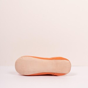 May include: Orange leather ballet flat. The shoe has a rounded toe and a flat sole. The sole is a light beige color, and the upper is a vibrant orange. The shoe is designed for comfort and style.
