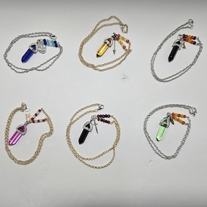 Puede incluir: Seis collares con colgantes de cristal hexagonal en azul, amarillo, negro, rosa, negro y verde. Cada colgante est&aacute; unido a una cadena de metal y decorado con peque&ntilde;as cuentas de colores y un peque&ntilde;o dije de metal con forma de espada o ancla.