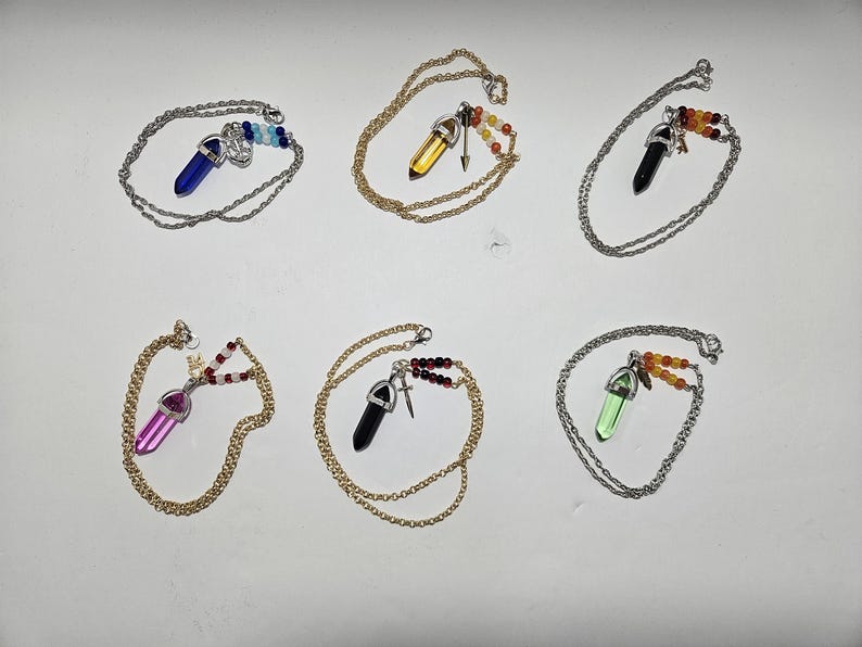 Puede incluir: Seis collares con colgantes de cristal hexagonal en azul, amarillo, negro, rosa, negro y verde. Cada colgante est&aacute; unido a una cadena de metal y decorado con peque&ntilde;as cuentas de colores y un peque&ntilde;o dije de metal con forma de espada o ancla.