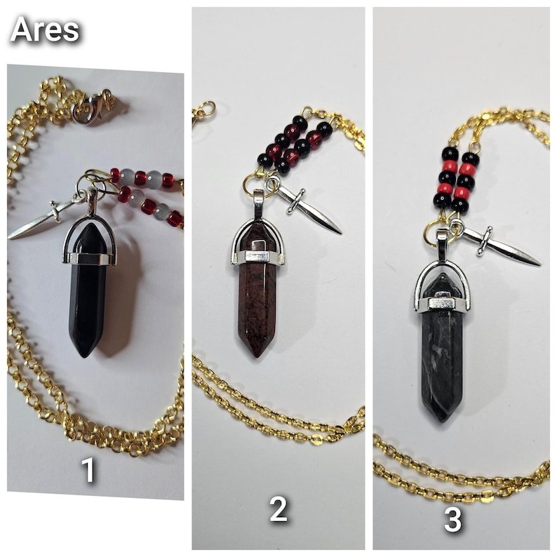 Puede incluir: Tres collares etiquetados como Ares, cada uno con cadena dorada, dije de espada plateado y colgante de cristal hexagonal. El collar 1 tiene un cristal negro y cuentas rojas, el 2 un cristal rojo oscuro y cuentas negras, y el 3 un cristal gris con cuentas.