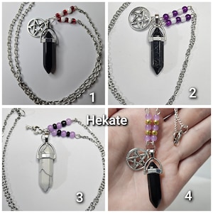 Puede incluir: Cuatro collares con cadenas plateadas, dijes de pent&aacute;culo y colgantes en forma de cristal. Los colgantes son negros o blancos con vetas. Las cadenas tienen cuentas rojas y blancas, moradas o negras y moradas. Una imagen muestra el texto Hekate.
