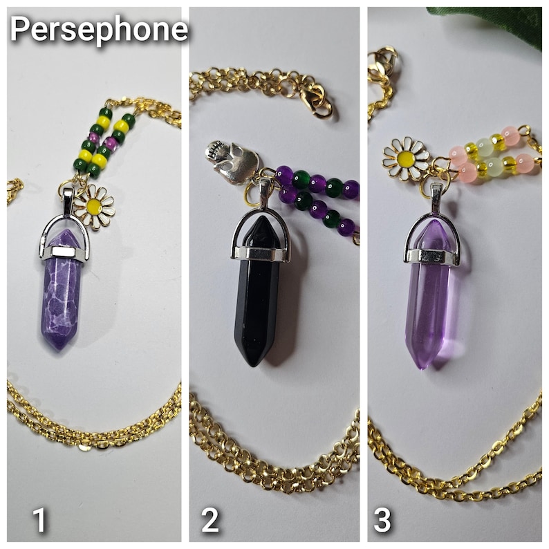 Puede incluir: Tres collares de cadena dorada con colgantes de cristal en punta. El collar 1 tiene una piedra morada, cuentas verdes y amarillas y un dije de margarita. El collar 2 tiene una piedra negra, cuentas moradas y verdes y un dije de calavera. El collar 3 tiene una piedra morada transparente, cuentas rosas y amarillas y un dije de margarita.