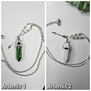 Puede incluir: Dos collares de tono plateado con un colgante de cristal en punta y un peque&ntilde;o dije de flecha. Un collar tiene un cristal verde oscuro y el otro un cristal blanco. Ambos incluyen peque&ntilde;as cuentas blancas en la cadena cerca del colgante.