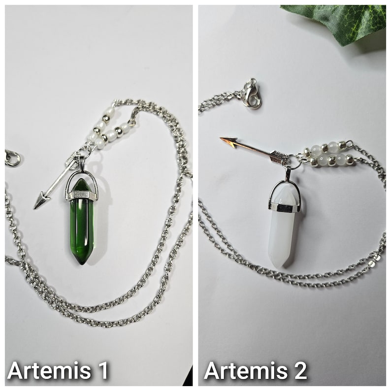 Puede incluir: Dos collares de tono plateado con un colgante de cristal en punta y un peque&ntilde;o dije de flecha. Un collar tiene un cristal verde oscuro y el otro un cristal blanco. Ambos incluyen peque&ntilde;as cuentas blancas en la cadena cerca del colgante.