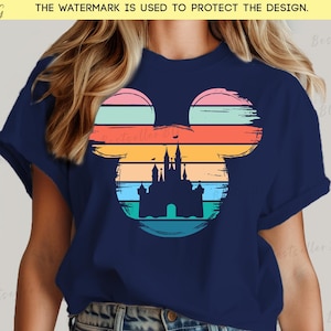 May include: Navy blue t-shirt featuring a colorful Mickey Mouse silhouette with a castle design. The design incorporates horizontal stripes in shades of pink, orange, yellow, and teal. The shirt is a classic crew neck.