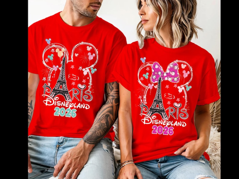 May include: Red t-shirts with a graphic featuring the Eiffel Tower, Mickey Mouse ears, and the text "Paris Disneyland 2026." One shirt has a bow. The shirts are worn by two people.