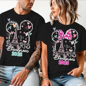 May include: Black t-shirts with a Disneyland Paris 2026 design. The design includes the Eiffel Tower, Mickey Mouse ears, fireworks, and the text "Paris Disneyland 2026". One shirt has a pink bow.