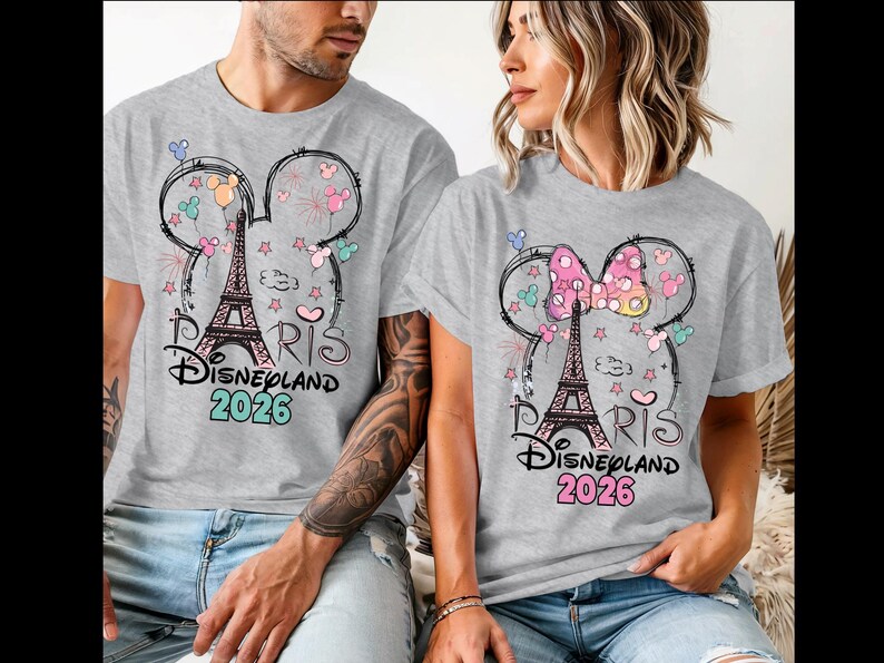 May include: Gray t-shirts featuring a design with the Eiffel Tower, Mickey Mouse ears, and the text "Paris Disneyland 2026." The design includes colorful balloons, stars, and fireworks. The shirts are worn by two people.