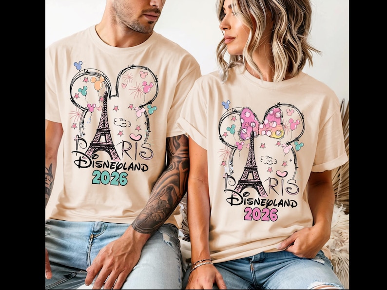 May include: Beige t-shirts featuring a Mickey Mouse head design with the Eiffel Tower, fireworks, and stars. The text "Paris Disneyland 2026" is printed below the design. One shirt has a bow.