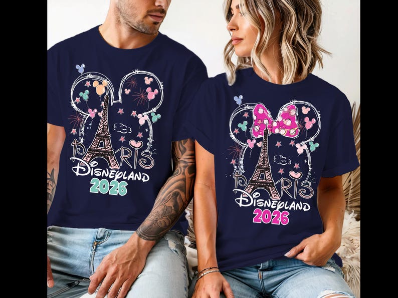 May include: Navy blue t-shirts with a Disneyland Paris 2026 design. The design includes the Eiffel Tower, Mickey Mouse ears, fireworks, and the word "Paris" in a script font. One shirt has a pink bow.