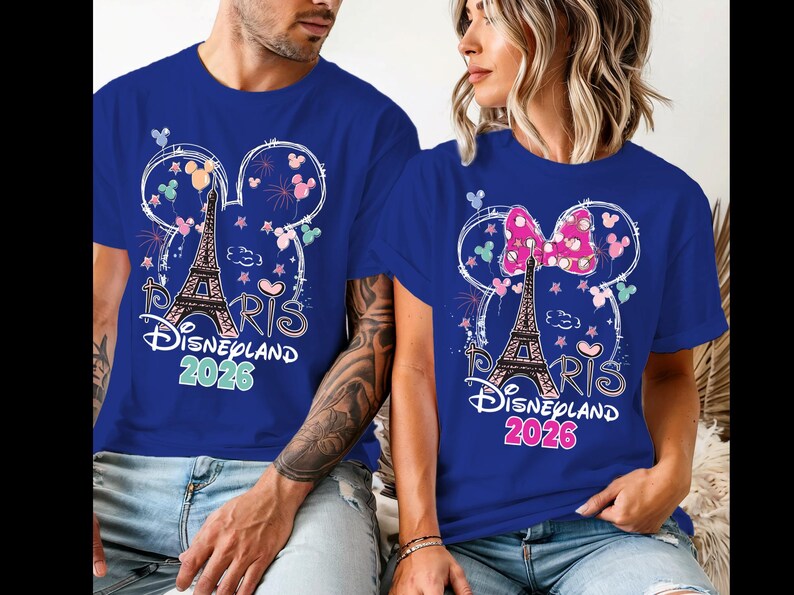May include: Two blue t-shirts with a Disneyland Paris 2026 design. The design includes the Eiffel Tower, Mickey Mouse ears, fireworks, and the word "Paris". One shirt has a pink bow.