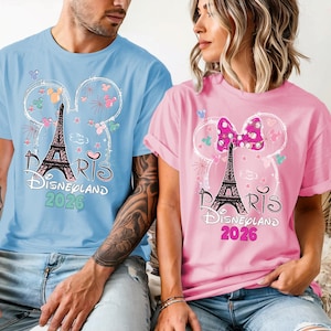 May include: Light blue and pink t-shirts with a graphic of the Eiffel Tower, Mickey Mouse ears, and the text "Paris Disneyland 2026." The shirts are short-sleeved and feature a whimsical design.