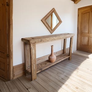 May include: A rustic wooden console table with a single shelf and a terracotta vase on the shelf. The table is in a room with white walls and wooden floors.