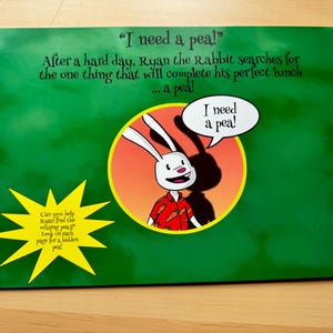 以下が含まれることがあります： 赤いニンジン柄の赤いシャツを着た、漫画のウサギが描かれた緑色の本の表紙。ウサギは「エンドウ豆が必要だ！」と言っています。本の表紙には、黄色い星形の吹き出しがあり、「ライアンが失くしたエンドウ豆を見つけるのを手伝ってくれる？ 隠されたエンドウ豆を各ページで見つけてね！」と書かれています。