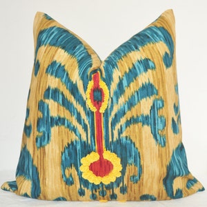 May include: A decorative throw pillow with a teal and gold ikat pattern. The pillow has a red and yellow embroidered design in the centre.