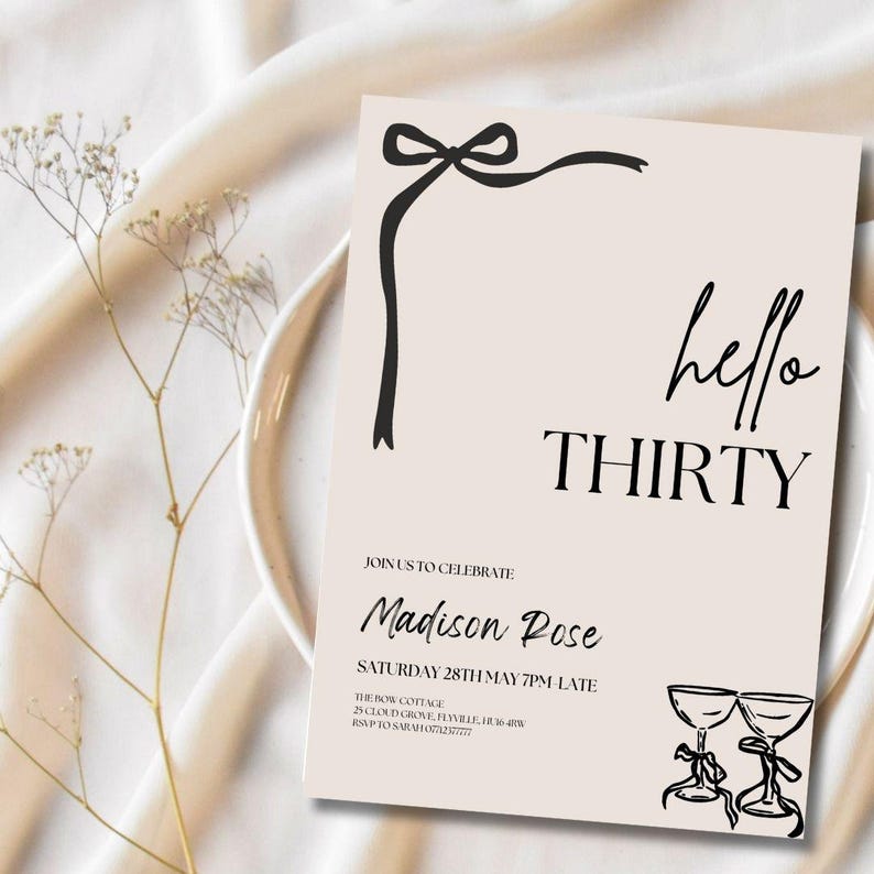 Puede incluir: Una tarjeta de invitaci&oacute;n de color melocot&oacute;n con texto negro y un dise&ntilde;o de lazo negro. El texto dice "hello THIRTY" e incluye detalles del evento. Dos copas de champ&aacute;n est&aacute;n ilustradas en la esquina inferior derecha. La tarjeta est&aacute; sobre un plato blanco y una tela crema.
