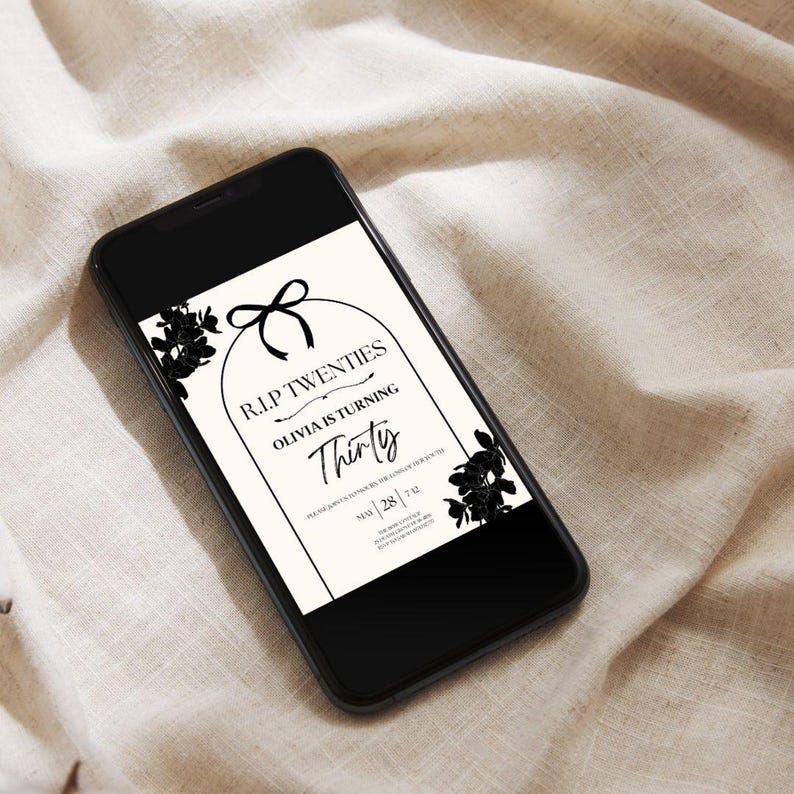 May include: A black smartphone displays a birthday invitation. The invitation features the text "R.I.P Twenties" and "Thirty" in a decorative font, with floral accents and a bow. The phone rests on a beige fabric surface.