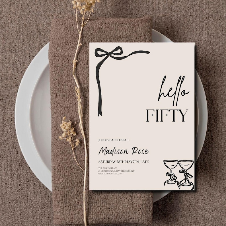 May include: A beige invitation card with the text "hello FIFTY" in black script. The card features a black ribbon design and two champagne glasses. The invitation is set on a white plate and a brown napkin.