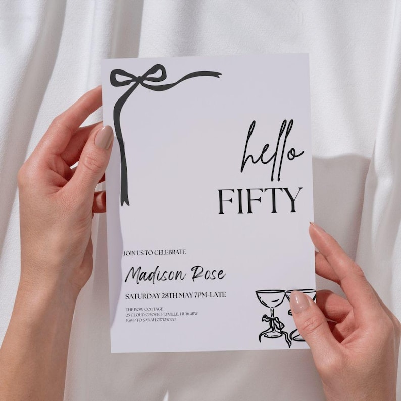 May include: A white invitation card with black text and illustrations. The card says "hello FIFTY" and includes event details. A black bow design is in the upper left corner. The card is held by two hands.