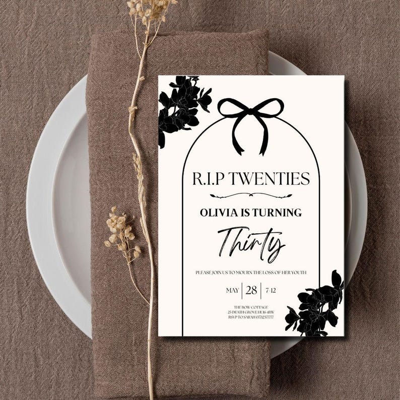 May include: A cream-colored invitation card with black floral accents and text. The text reads "R.I.P Twenties, Olivia is turning Thirty." The card is placed on a brown napkin and white plate, with dried flowers.