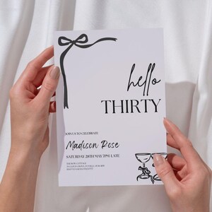Puede incluir: Una tarjeta de invitaci&oacute;n blanca con texto e ilustraciones en negro. Las palabras "hello THIRTY" se muestran de forma destacada. La tarjeta incluye detalles para una celebraci&oacute;n, con un lazo y dos copas de champ&aacute;n ilustradas.