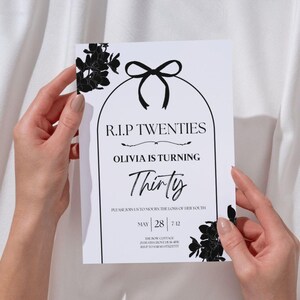 May include: A white invitation card with black text and floral accents. The card reads "R.I.P. TWENTIES, OLIVIA IS TURNING Thirty." Includes event details: May 28, 7-12, and RSVP information. The card is held by two hands.