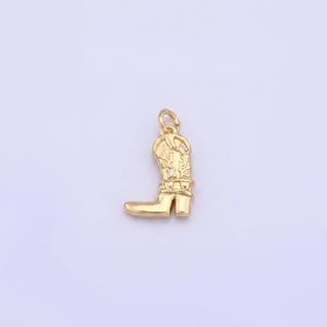 May include: A gold-colored charm in the shape of a cowboy boot. The boot has intricate detailing on the shaft and a small loop at the top for attaching to a chain or bracelet. The charm is a miniature representation of a classic Western boot.