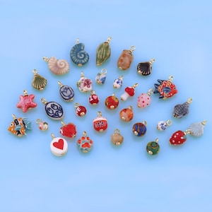 以下が含まれることがあります： 花、魚、貝殻、星、ハート、キノコなど、さまざまなデザインのカラフルなセラミックチャームのコレクション。チャームはすべて小さく、ジュエリーやその他のクラフトに取り付けるための金色の金属ループが付いています。