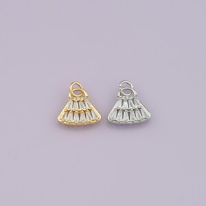 May include: Two pendant charms, one gold-toned and one silver-toned, each shaped like a stylized dress. The charms are adorned with clear, baguette-cut crystals. Each charm has a small loop at the top for attaching to a chain or bracelet.