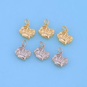 May include: Six chef hat charms in gold and silver tones. The charms are small, with a detailed design of a classic chef's hat. Each charm has a small loop at the top for attaching to a chain or bracelet. The background is a solid light blue.