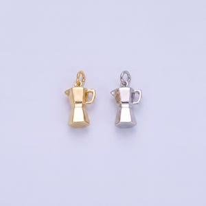 May include: Two small metal charms shaped like moka pot coffee makers. One charm is finished in a polished gold tone, and the other charm is finished in a polished silver tone. Each charm features a small circular jump ring at the top for attachment.