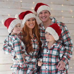 Op de afbeelding: Een gezin van vier personen draagt bijpassende rood-wit geruite pyjama's met kerstmanmutsen. De mutsen zijn gebreid met witte pompoenen.