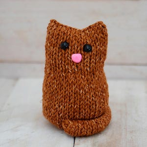 May include: A brown knitted cat toy with black eyes and a pink nose.