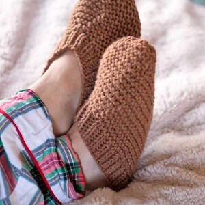 May include: A pair of brown knitted slipper socks with a textured knit pattern. The socks are being worn on someone's feet.
