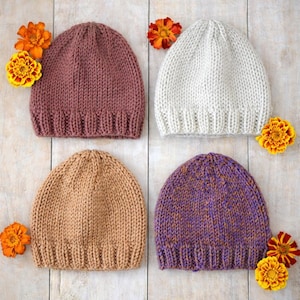 May include: Four knitted beanies in shades of mauve, cream, tan, and purple with orange and yellow flowers. The beanies are made of a thick, textured yarn and have a ribbed brim.