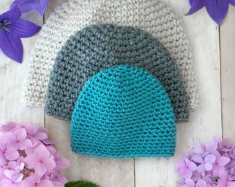 May include: Three crocheted hats in different sizes, stacked on top of each other. The top hat is teal, the middle hat is gray, and the bottom hat is white.