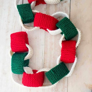 Könnte beinhalten: Eine gestrickte Weihnachtsgirlande mit roten, grünen und weißen Schlaufen. Die Girlande ist aus Garn gefertigt und perfekt, um ein Zuhause für die Feiertage zu dekorieren.