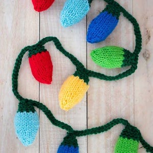 May include: A string of knitted light bulbs in red, blue, green, yellow, and light blue. The bulbs are connected by a green knitted cord.