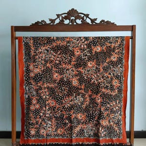 Könnte beinhalten: Ein schwarzes Textil mit einem Blumenmuster in Rot und Weiß wird auf einem Holzgestell präsentiert. Das Textil hat einen roten Rand mit weißen Punkten. Das Gestell hat eine dekorative Oberseite. Das Textil ist wahrscheinlich ein dekoratives Tuch oder Stoff.