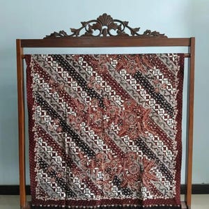 Könnte beinhalten: Ein brauner und weißer Batikstoff mit geometrischem Muster wird auf einem Holzständer präsentiert. Der Stoff hat ein diagonales Muster aus weißen, schwarzen und braunen Linien.