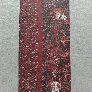 Może przedstawiać: Tkanina batik w kolorze bordowym z kwiatowym wzorem w kolorze czarnym i białym. Tkanina ma subtelny połysk i przyjemną fakturę.