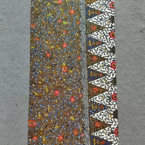 Puede incluir: Una tela batik marrón y azul con un borde blanco que presenta un patrón geométrico. La tela tiene un diseño floral con acentos rojos, amarillos y verdes.