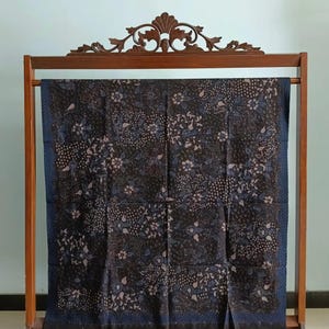 Peut inclure: Un tissu batik noir et bleu avec un motif floral. Le tissu est présenté sur un support en bois.