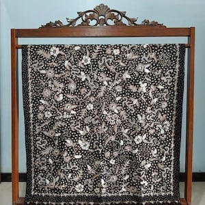 May include: A black and white batik fabric with a floral pattern. The fabric is displayed on a wooden stand.