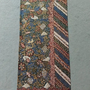 Könnte beinhalten: Ein rechteckiges Stoffpanel mit einem farbenfrohen Batik-Muster. Das Muster zeigt ein florales Design in den Farben Blau, Grün, Gold und Rot. Der Stoff hat eine glatte Textur.